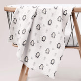 Arctic penguin print muslin swaddle draped over wooden baby stand